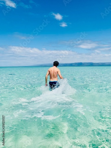 A man walking in the shallow ocean with turqouise blue water at summer.