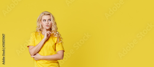 Photo of a happy young blond woman standing isolated over yellow wall background. Looking at the camera showing the direction of copy space. Banner