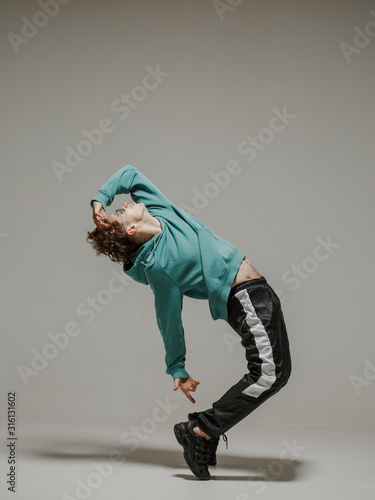 Guy dancing contemporary dance in studio. Neutral grey background. Acrobatic bboy dancer.