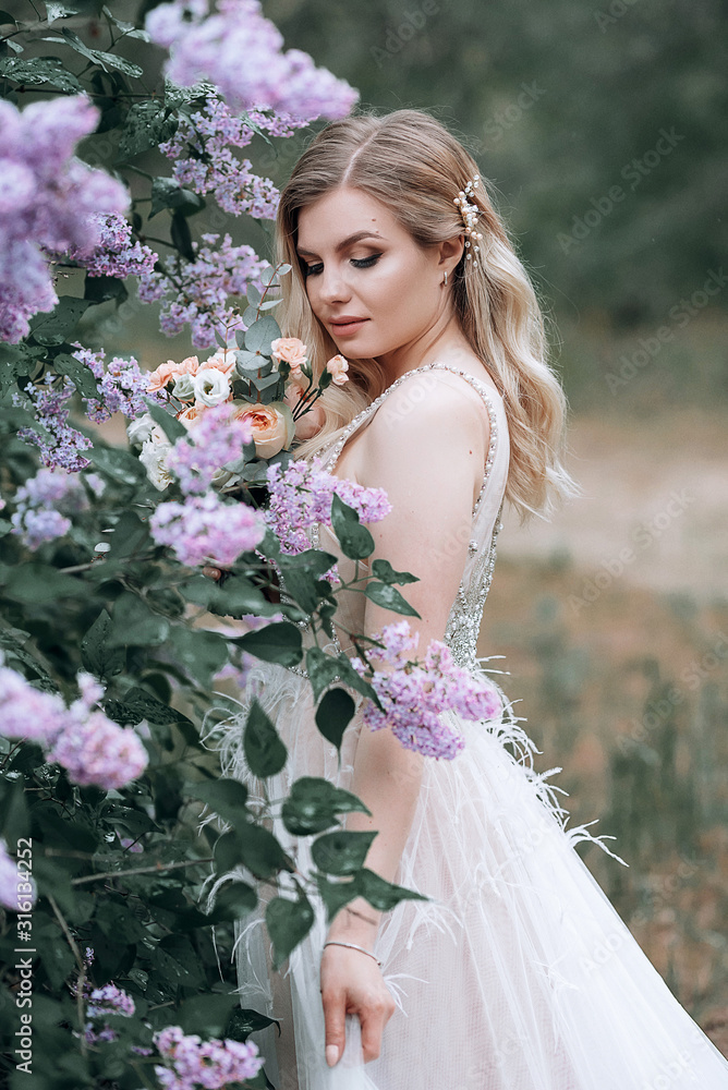young beautiful bride with a wedding bouquet near lilac bushes
