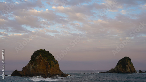 volcanic mountainous islands in the blue water of the Pacific Ocean. tropical islands of Japan overgrown with green plants against a beautiful sunset sky. Aburatsu