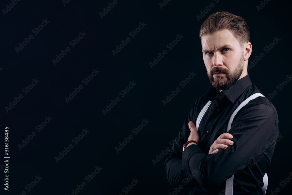 Half-turned portrait of masculine bearded man in black shirt and white suspenders isolated black background copyspace Half-turned portrait of masculine bearded man in black shirt and white suspenders isolated black background copyspace