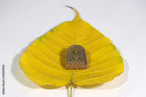 Small buddha amulet on yellow sacred fig or Bodhi leaf on white floor. photo