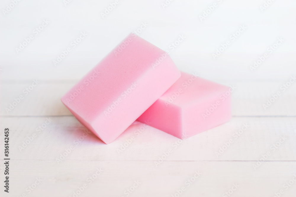 Two pink melamine rectangular sponges on a white wooden table. Useful household cleaning tools Two pink melamine rectangular sponges on a white wooden table. Useful household cleaning tools