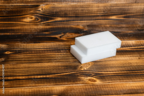 Two white melamine rectangular sponges on a wooden table. Useful household cleaning tools
