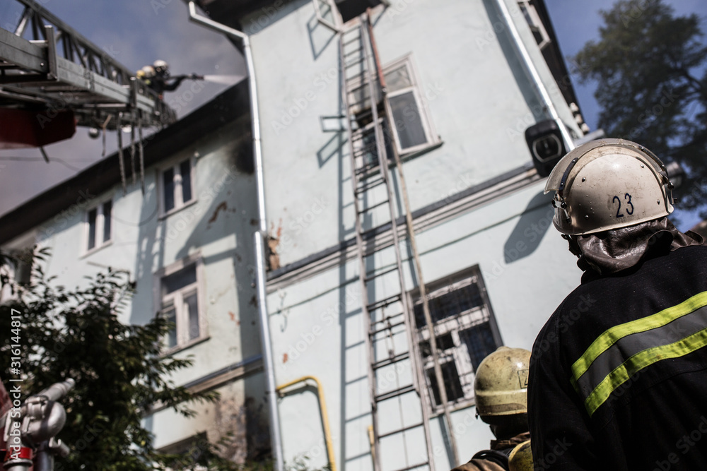 Firefighters on ladders in oxygen masks extinguish the fire in an old house in the middle of the city Firefighters on ladders in oxygen masks extinguish the fire in an old house in the middle of the city