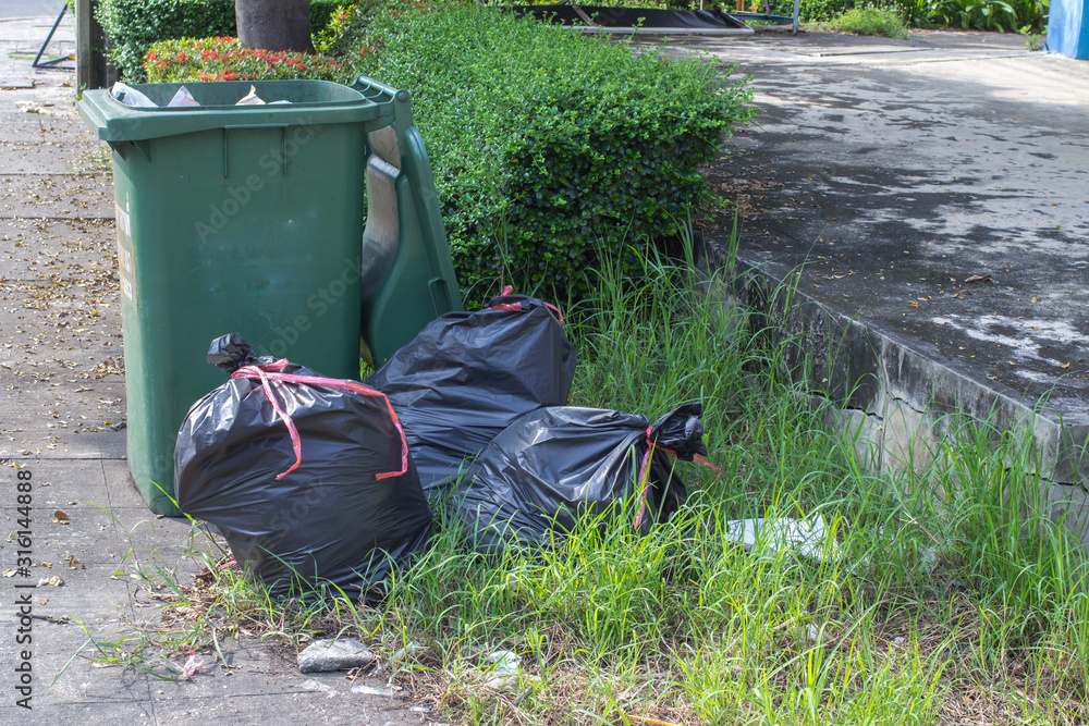 large green wheelie bin for rubbish,Public trash background,Big pile of garbage and waiste in black bags. large green wheelie bin for rubbish,Public trash background,Big pile of garbage and waiste in black bags.