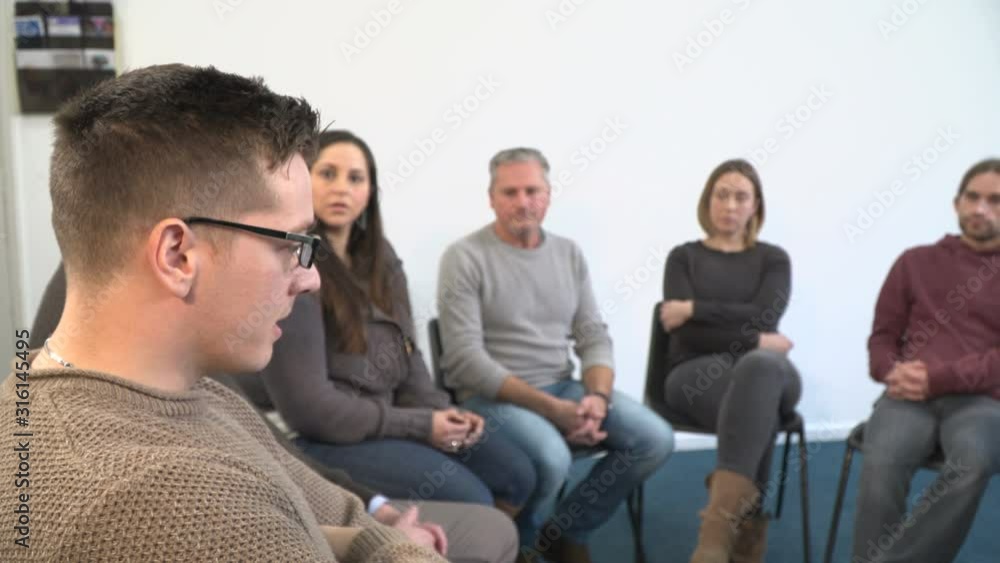 4K: Support group therapy - People sat in circle for a recovery meeting - One man talks while the others listen. 4K: Support group therapy - People sat in circle for a recovery meeting - One man talks while the others listen.