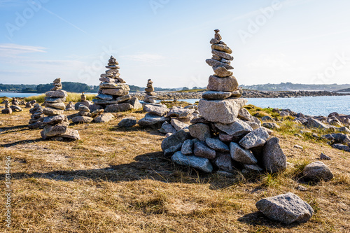 Many man-made granite stone stacks (called cairns) on the coastal path in Brittany, France, on a sunny late afternoon.