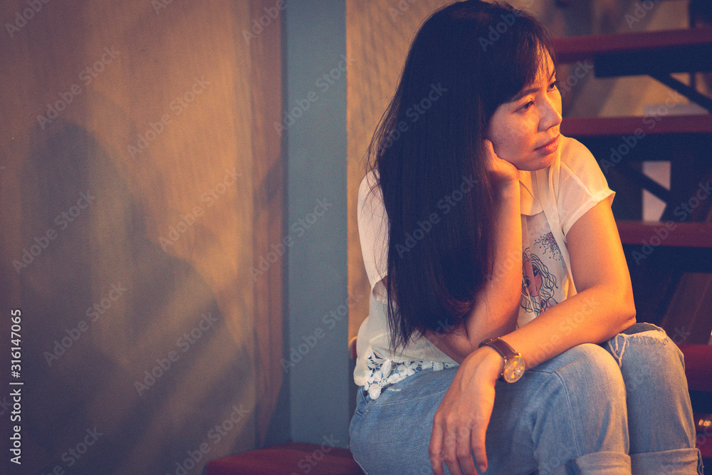 Young Asian woman sitting on the stairs in a lonely mood. Process in retro vintage style old film and add some noise grain. Young Asian woman sitting on the stairs in a lonely mood. Process in retro vintage style old film and add some noise grain.