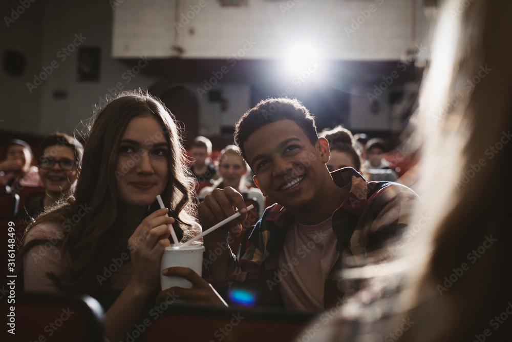 Tween couple watching movie, sharing soda with straws in movie theater