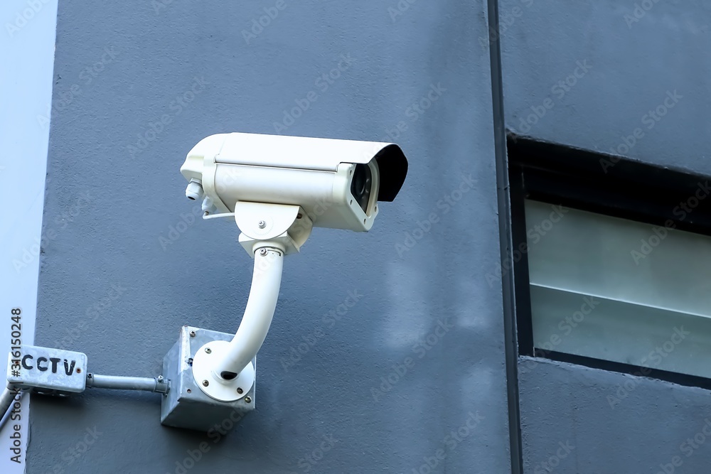 Beside view of white cctv camera on the corner of dark gray building.