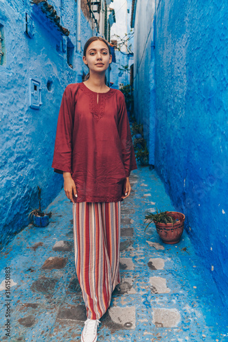 narrow corridor of the street of the blue city of morocco and in it stands a girl in a blouse and pants © nelen.ru