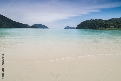 view of white sand beach and blue-green sea with mountains background, Krating beach, Surin island, Mu Ko Surin National Park, Phang Nga, southern of Thailand.