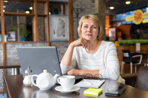 A woman with a laptop looks at a document in a cafe, office