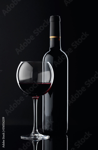 Bottle and glass of red wine on a black background.