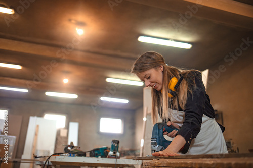 Woman craftswoman working in her workshop. Portrait view of happy attractive hardworking middle aged professional female carpenter working in the workshop or garage.