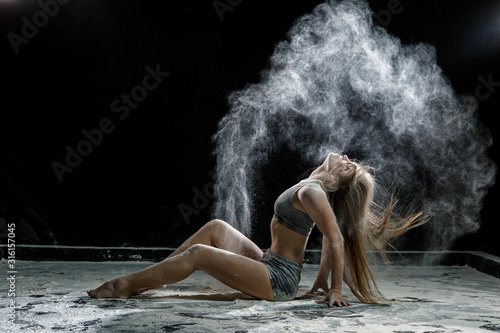 Fototapeta Naklejka Na Ścianę i Meble -  Beautiful girl model on a black background throws flour