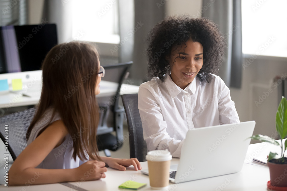 Female colleagues discuss ideas working at laptop together Female colleagues discuss ideas working at laptop together