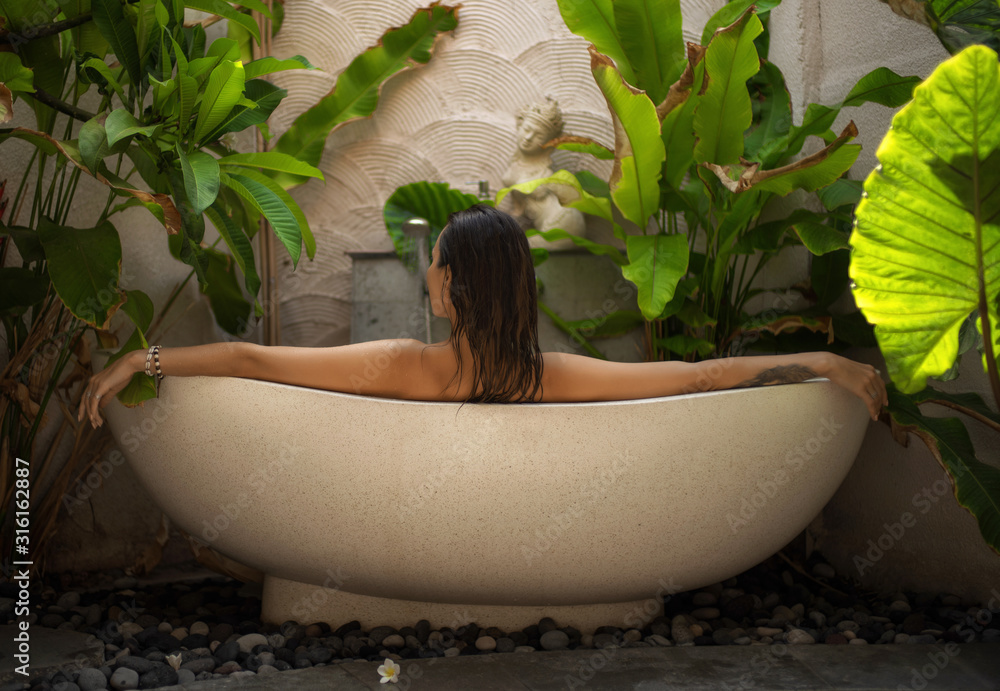 Woman relaxing in outdoor bath with tropical leaves at Bali - obrazy, fototapety, plakaty 