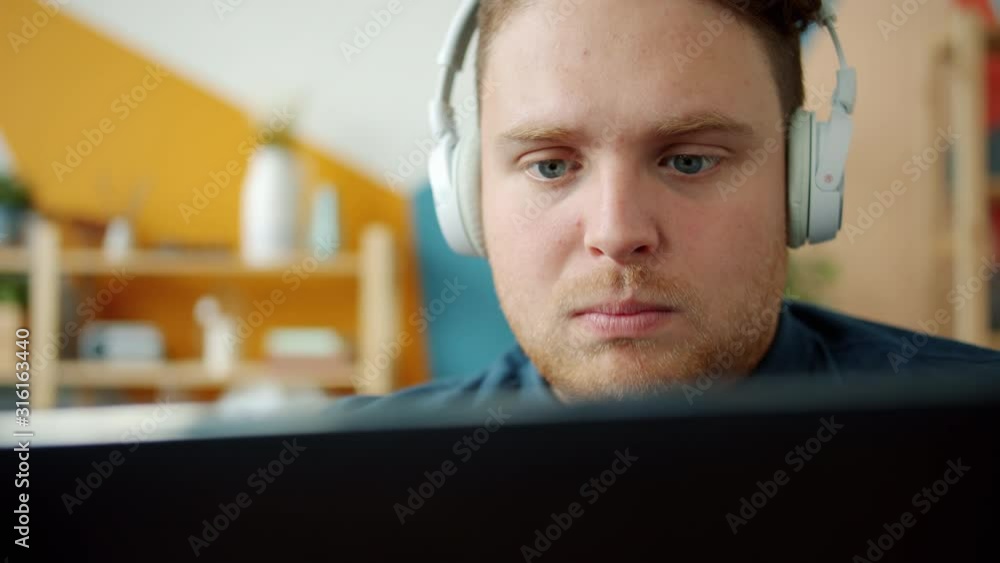 Smiling student wearing headphones is enjoying music and using tablet in apartment with happy face. Modern technology, house and joyful youth concept. Smiling student wearing headphones is enjoying music and using tablet in apartment with happy face. Modern technology, house and joyful youth concept.