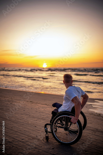 Handicapped man in wheelchair and his girlfriend alone on a beach at sunset