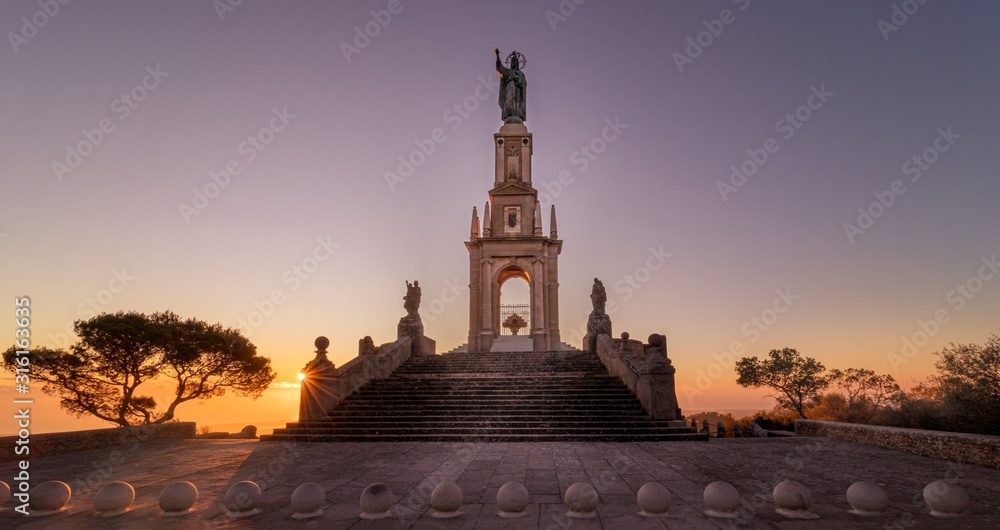 Statue of Christ, Sant Salvador church at sunrise with beautiful colourful sky and sun flare located near Felanitx, Mallorca, Spain.