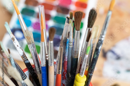  Paint brushes and watercolor paints, tempera paints on the table in a workshop, selective focus, close up, on wooden background.