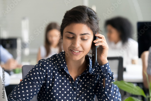 Smiling female employee talk over phone at shared workplace