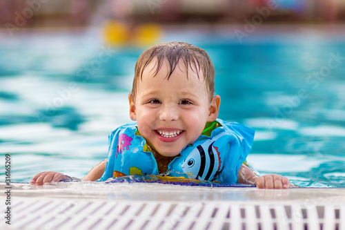 Cute three year old boy in a life jacket near the pool in summer on vacation at the hotel.