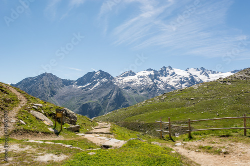 Mountain hiking paths across green pastures through wide valley.