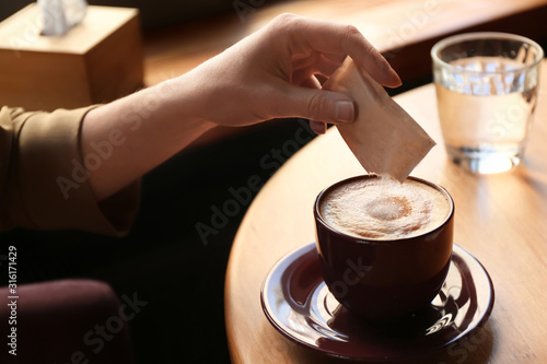 Woman adding sugar to aromatic coffee at table in cafe, closeup