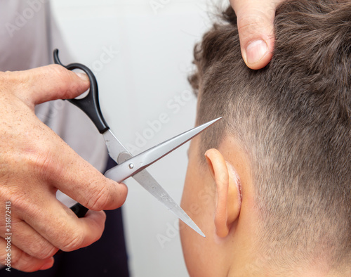 The hairdresser cuts the boy’s ear with scissors