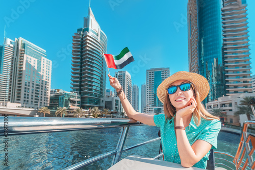 Photography Asian girl waving UAE flag on a boat cruise ship with skyscrapers of Marina port