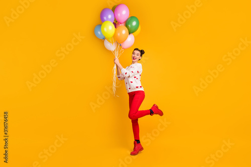 I m gonna fly. Full length profile photo of beautiful lady bring many colorful air balloons surprise party wear hearts pattern sweater red pants shoes isolated yellow color background