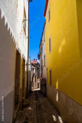 Narrow street with yellow colored walls of Lisbon on a summer day with blue sky