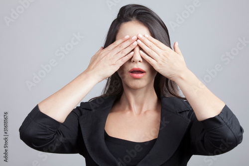 ragazza vestita con giacca nera si copre gli occhi isolata su sfondo grigio photo