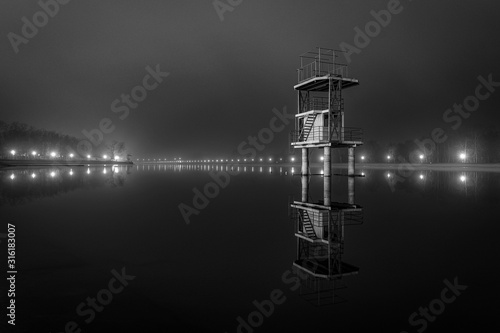Fine art black and white misty night photo of rowing channel with tower in water