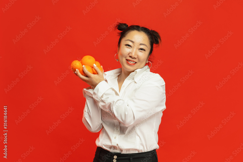 Taste of holidays. Happy Chinese New Year 2020. Asian young woman holding mandarines on red background in traditional clothing. Smiling, cute, happy. Celebration, human emotions, holidays. Copyspace. Taste of holidays. Happy Chinese New Year 2020. Asian young woman holding mandarines on red background in traditional clothing. Smiling, cute, happy. Celebration, human emotions, holidays. Copyspace.
