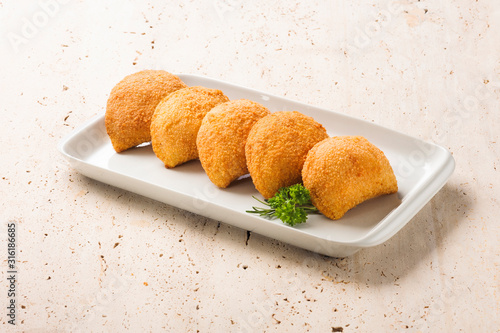 Five rissoles, a small patty enclosed in pastry, or rolled in breadcrumbs, usually baked or deep fried, filled with savory ingredients. On a white plate. photo