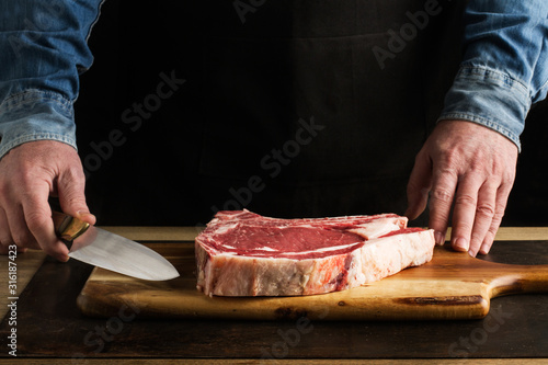 Canvastavla Hombre preparando chuletón de vaca con cuchilla sobre tabla de madera rústica