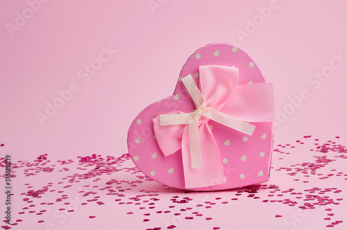 closed pink gift box in the form of a heart with a bow on a pink background