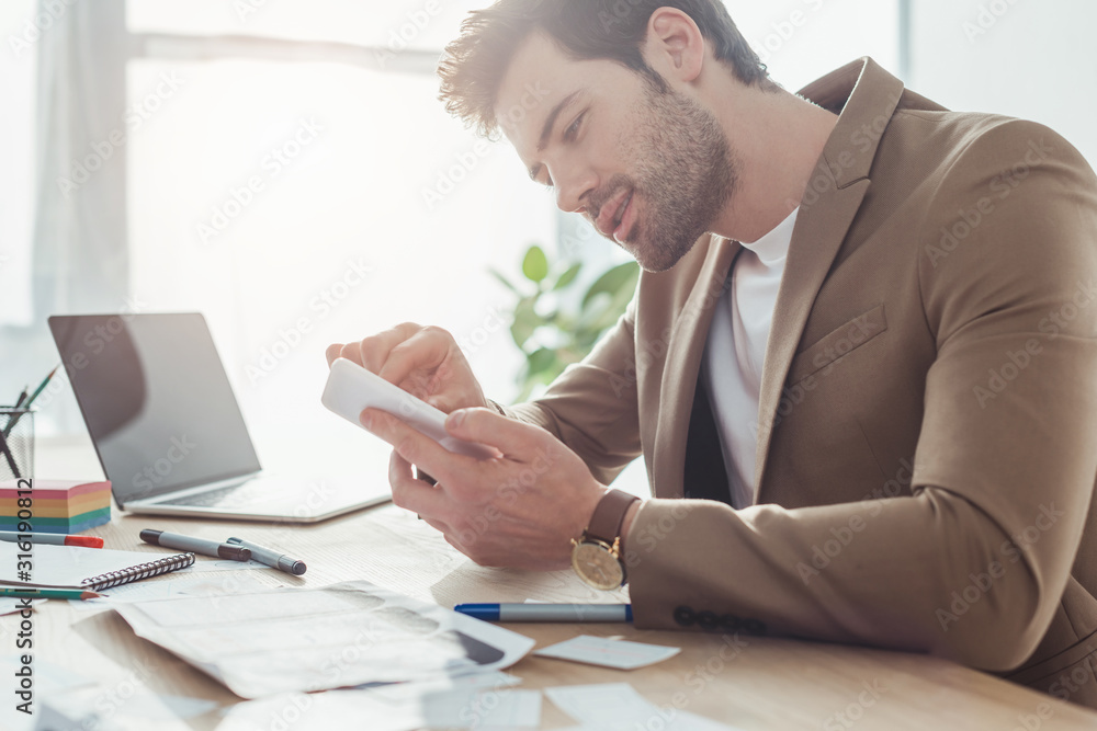 Side view of designer using smartphone with ux app sketches on table Side view of designer using smartphone with ux app sketches on table