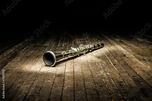 a black woodwind clarinet lies on a dark brown wooden stage in the rays of light photo