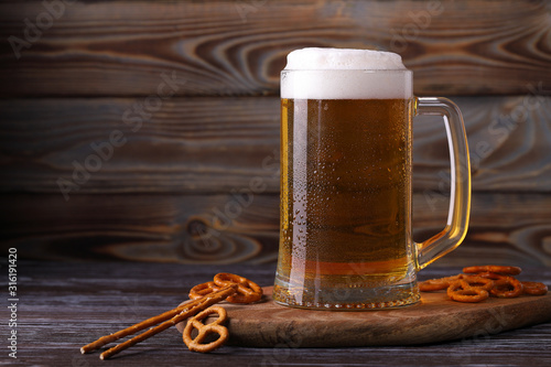 A large mug of cold, fresh, tasty, lager beer with foam and a snack of salted pretzels and sticks.
