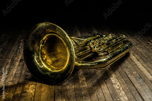 golden brass wind instrument euphonium lies on a brown wooden stage in the light of a spotlight photo