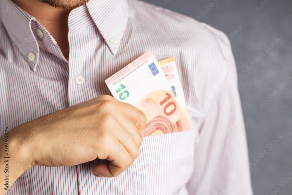 Close up hand of a man in a striped shirt holding 10 euro banknote into pocket. businessman puts money out of his breast pocket Close up hand of a man in a striped shirt holding 10 euro banknote into pocket. businessman puts money out of his breast pocket