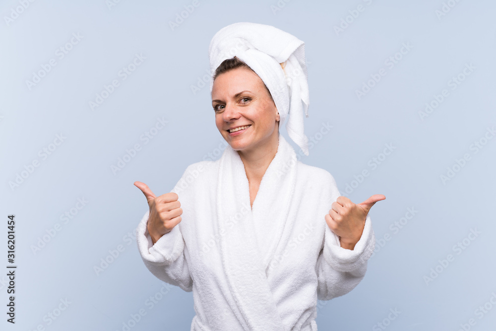 Woman in bathrobe over isolated blue background giving a thumbs up gesture Woman in bathrobe over isolated blue background giving a thumbs up gesture