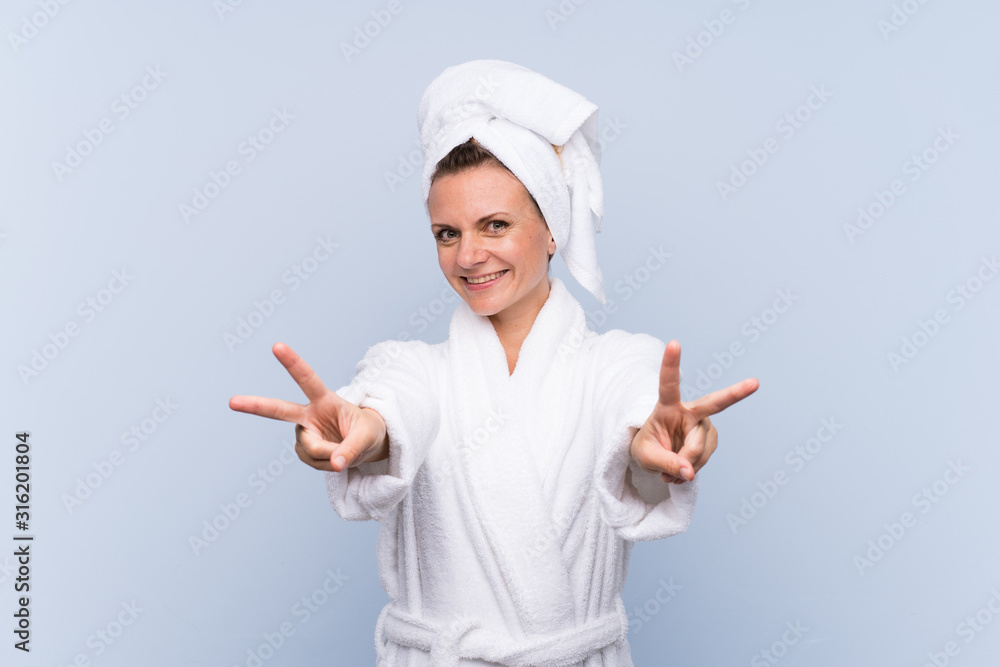 Woman in bathrobe over isolated blue background smiling and showing victory sign Woman in bathrobe over isolated blue background smiling and showing victory sign