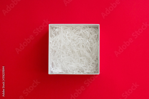 open box with filling material inside lying on a red colored paper background, top view